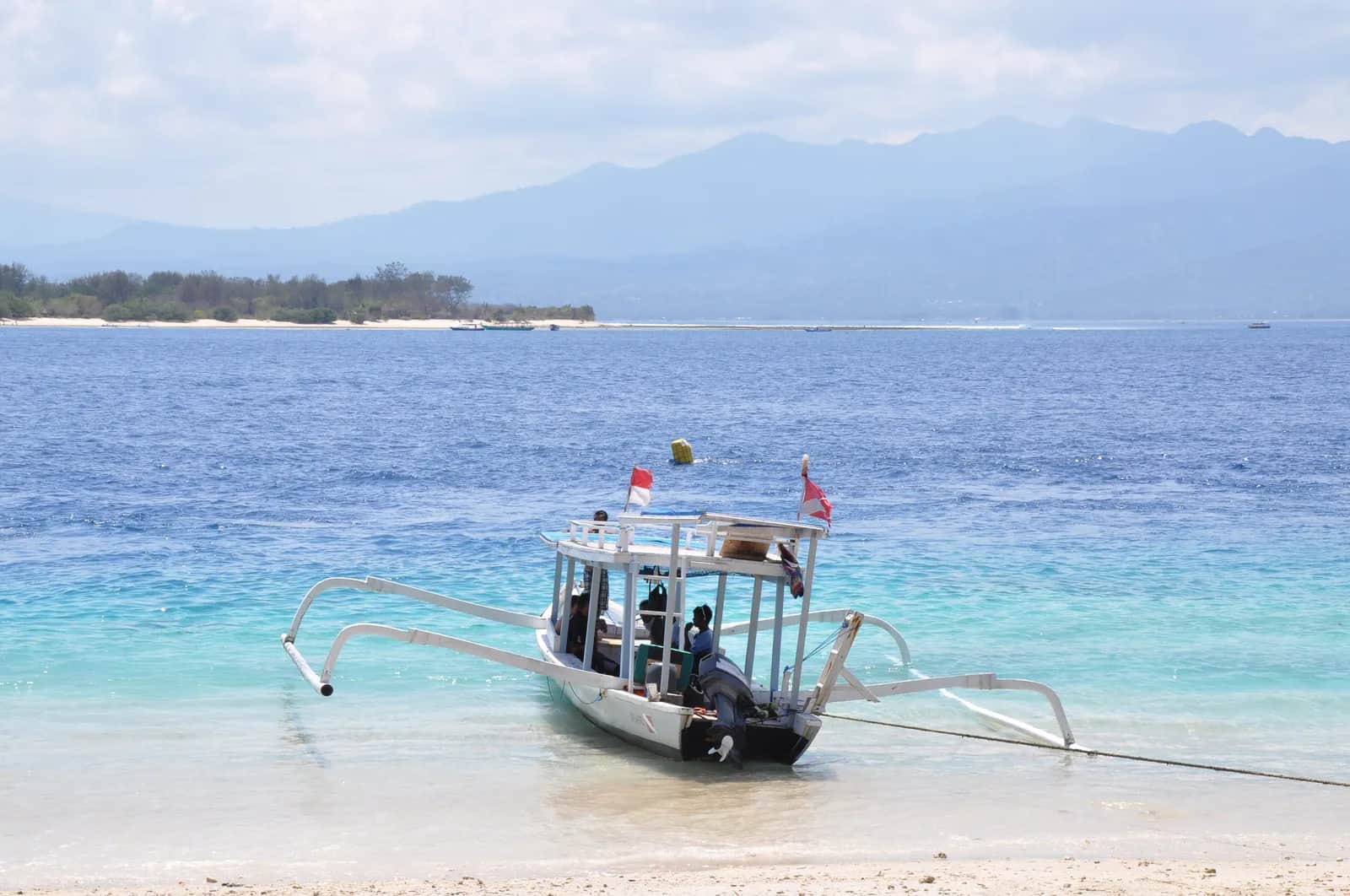 Bateau traditionnel à balancier sur une plage de Gili Trawangan, avec Lombok au fond