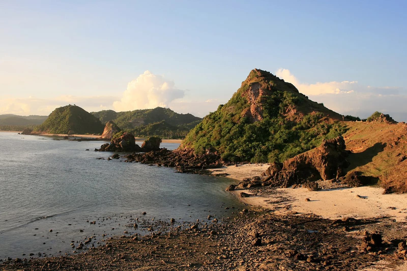Collines vertes et petite baie de sable près de la plage de Seger, à côté de Kuta Lombok, au coucher du soleil