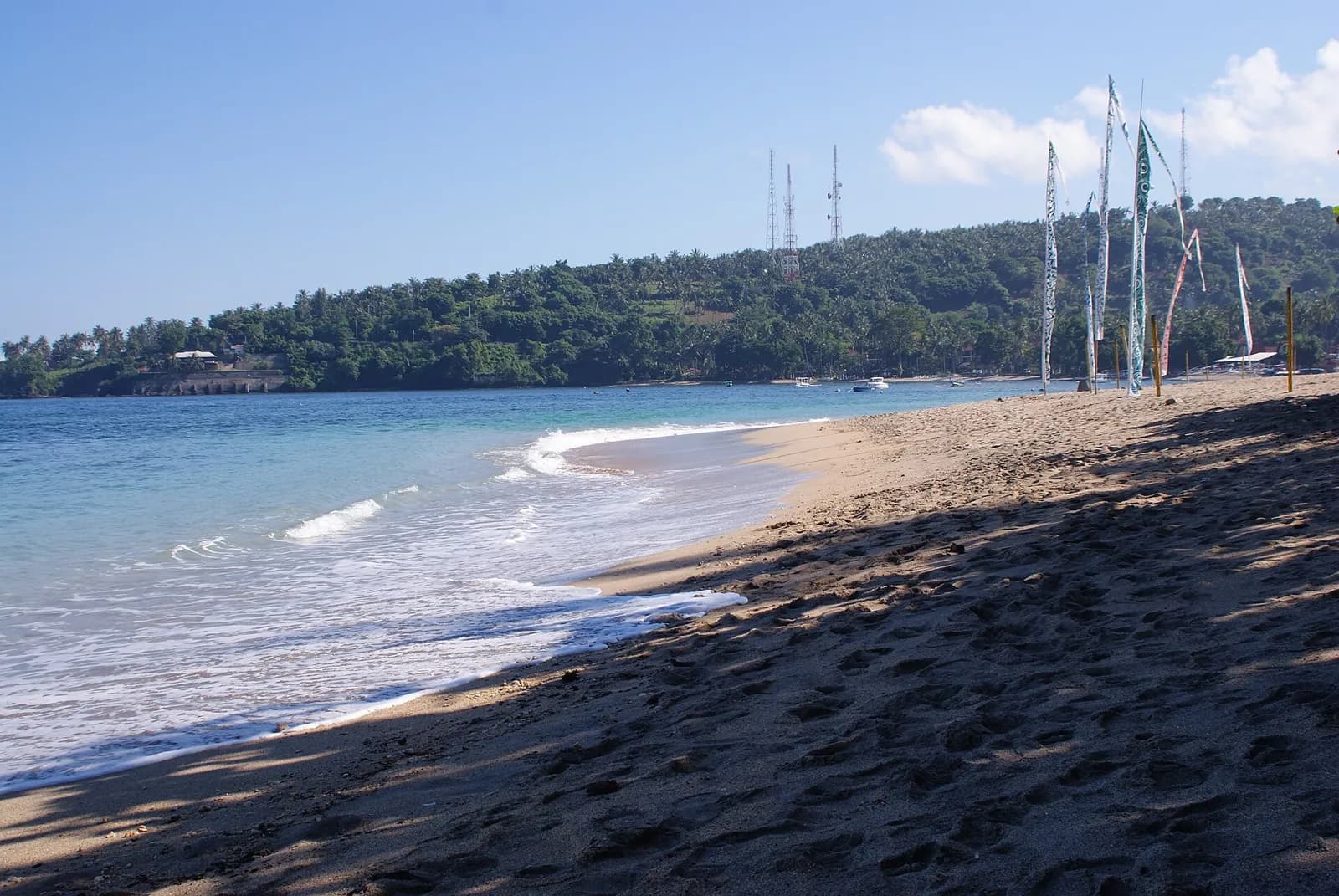 Plage de sable gris de Senggigi, sur la côte ouest de Lombok, avec les collines boisées au fond