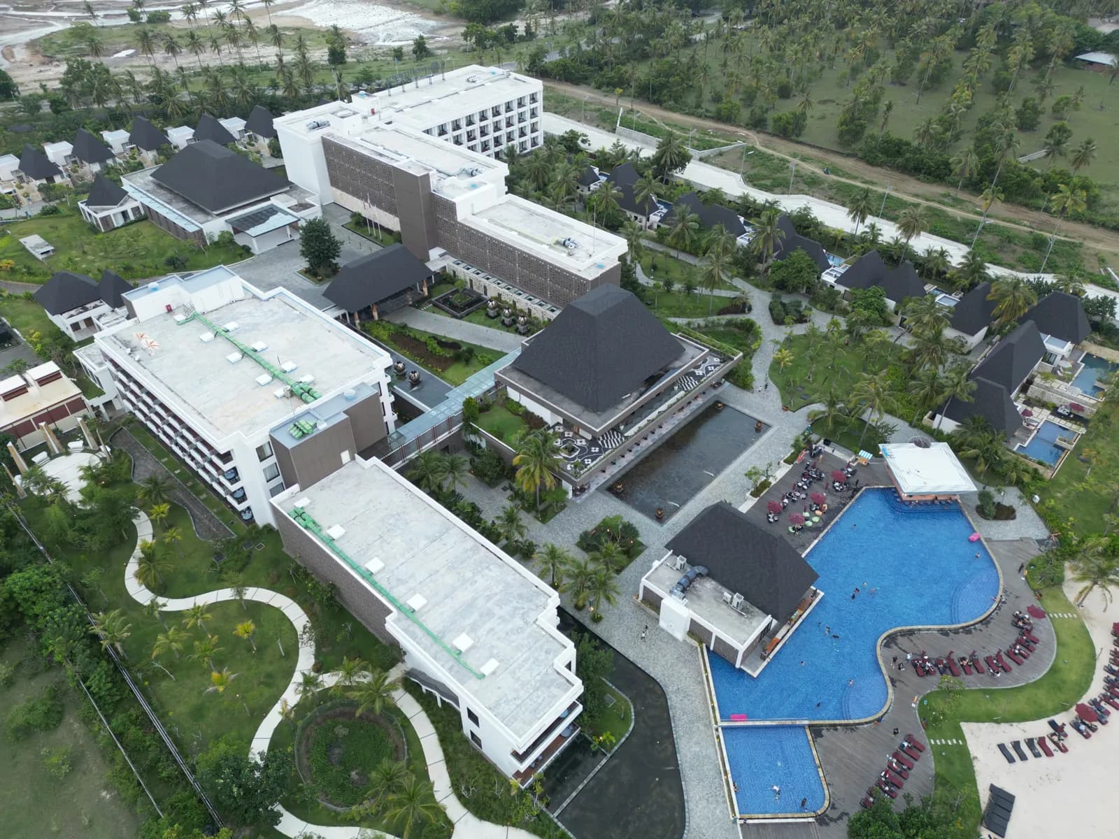 Vue aérienne d'un resort avec piscine et bâtiments à toits sombres à Mandalika, sur la côte sud de Lombok