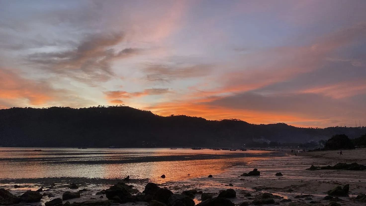 Coucher de soleil sur la plage de Kuta Mandalika, au sud de Lombok, avec les collines qui se détachent sur un ciel orangé