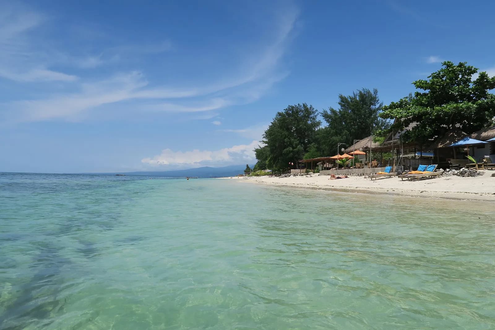 Eau turquoise et plage bordée d'arbres et de paillotes sur la côte ouest de Gili Air