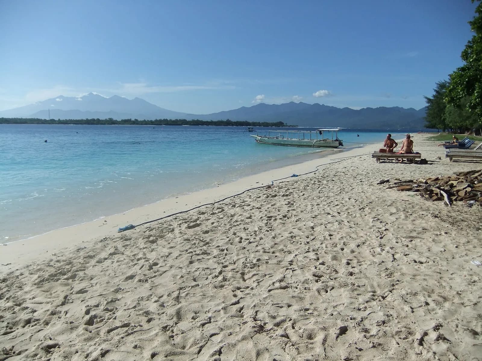 Plage de sable clair à Gili Trawangan, avec une pirogue et les montagnes de Lombok à l'horizon