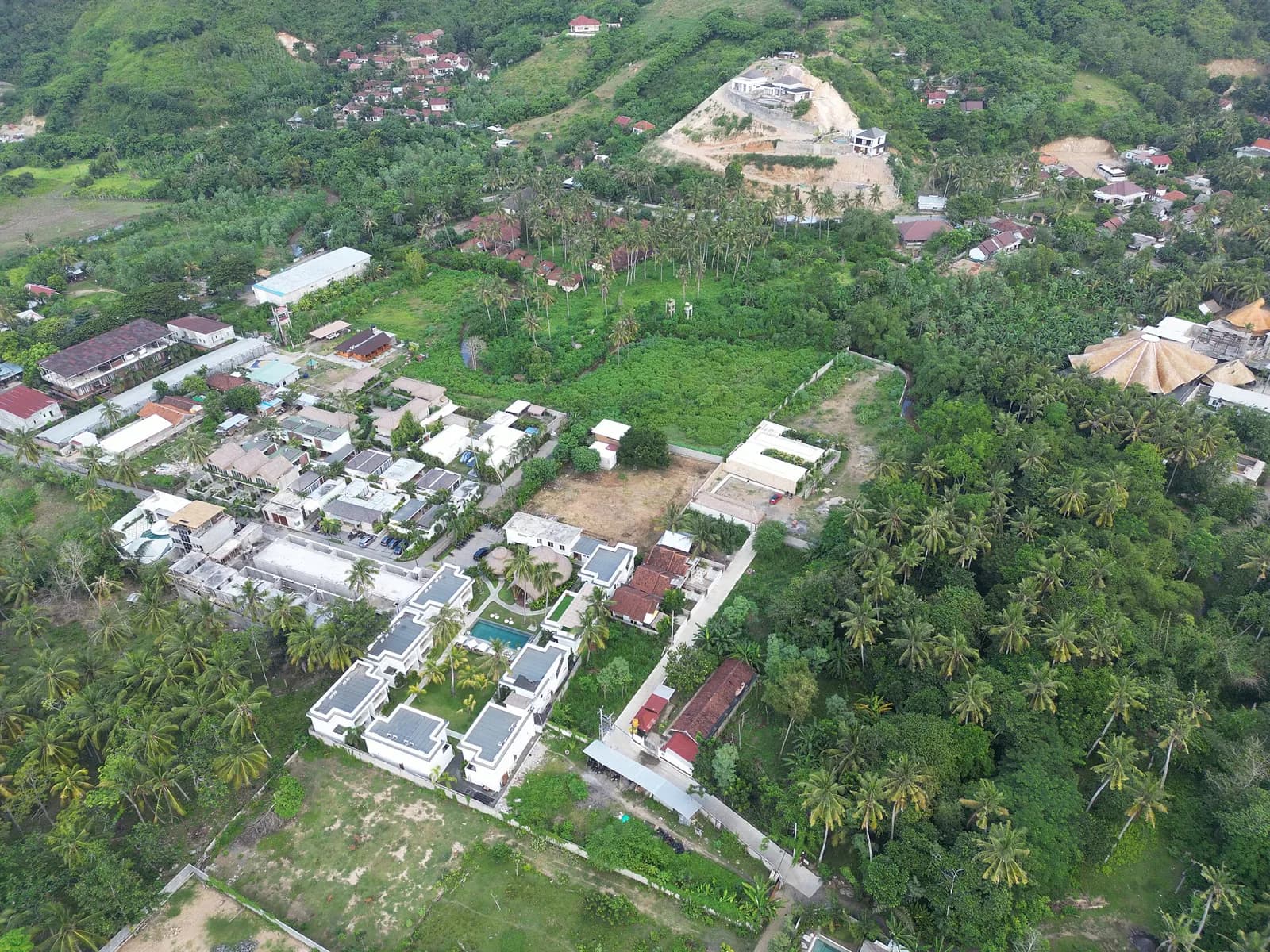 Vue aérienne d'un ensemble de villas modernes à toit plat, avec une piscine, entouré de cocotiers à Kuta, Lombok