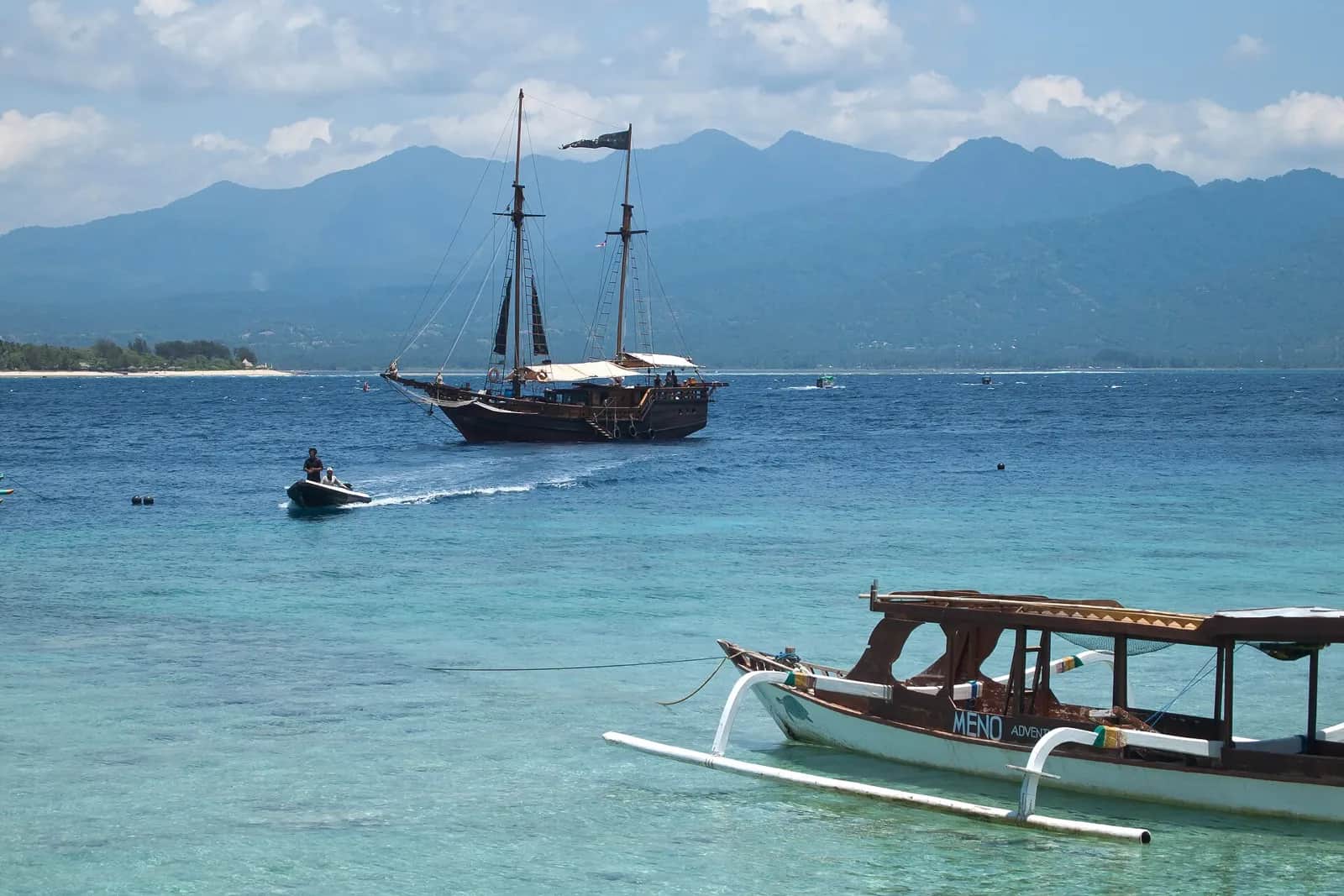 Voilier et bateau à balancier sur la mer turquoise devant Gili Meno, avec les montagnes de Lombok au fond