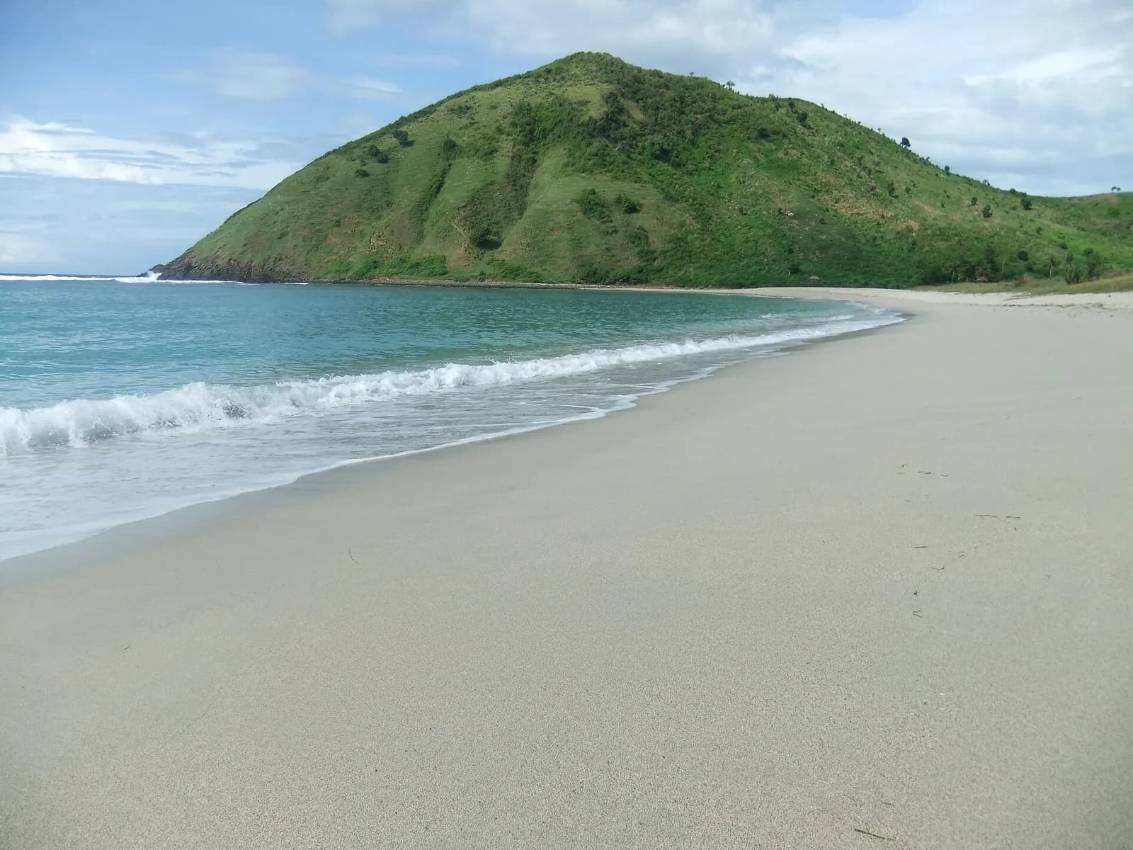 Plage de Mawun, au sud de Lombok : baie de sable clair en arc de cercle, bordée d'une colline verte