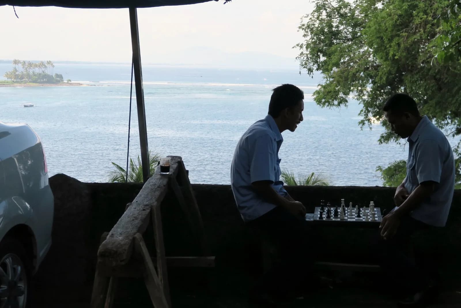 Deux chauffeurs de taxi jouant aux échecs au bord d'une route côtière de Lombok, face à la mer