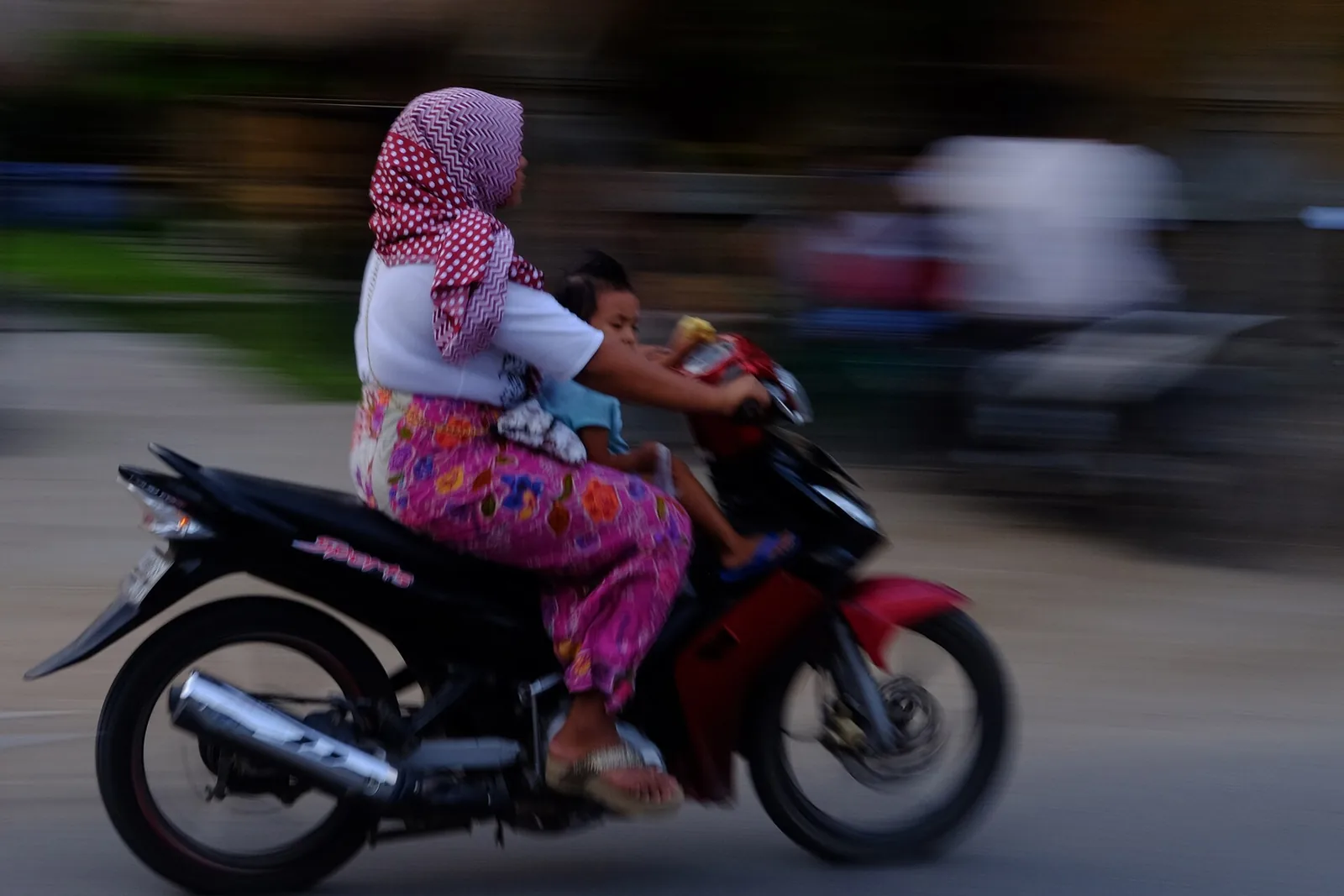 Une femme et un enfant sur un scooter en mouvement dans une rue de Kuta, Lombok