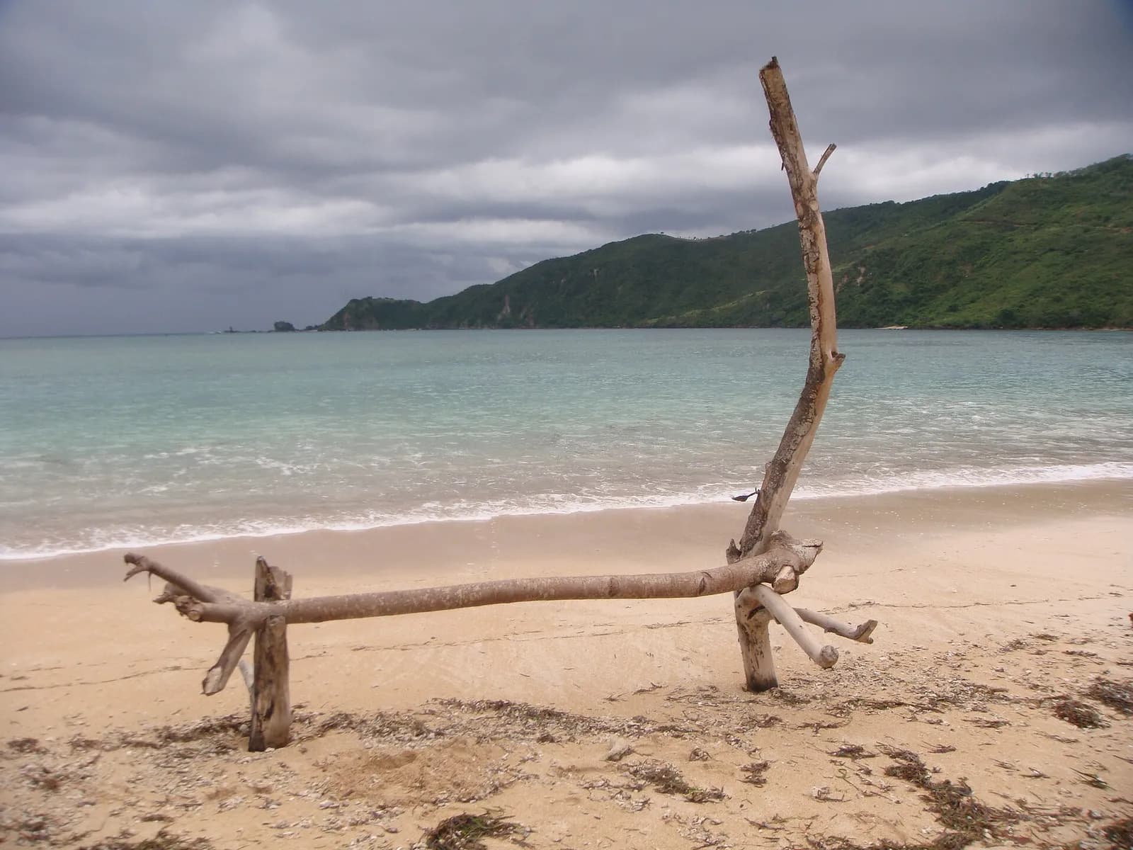 Plage de sable clair de Kuta Mandalika, à Lombok, avec un tronc de bois flotté et une colline verte au fond