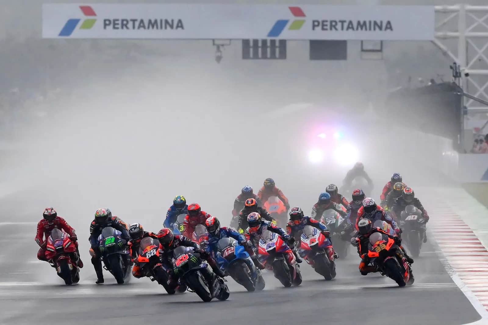 Départ groupé des pilotes MotoGP sous la pluie, devant l'arche Pertamina, au circuit de Mandalika à Lombok