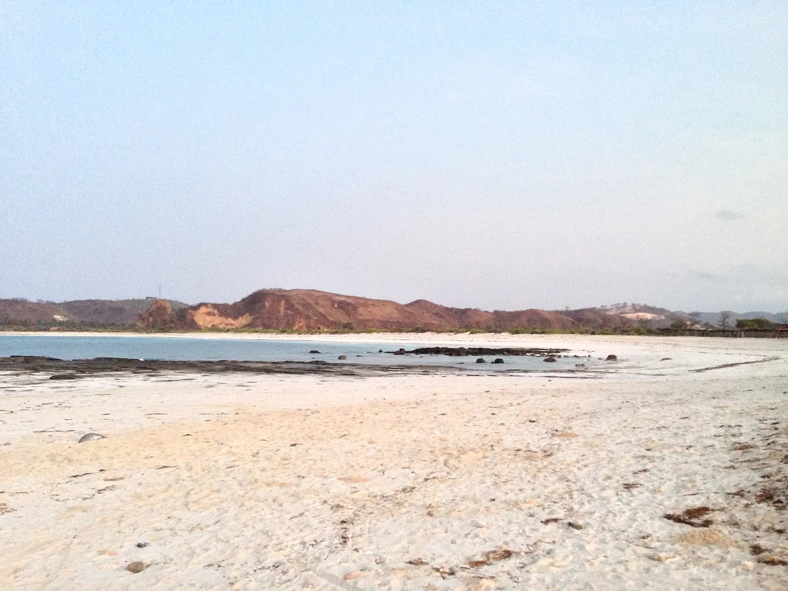 Plage de sable blanc de Kuta, à Lombok, avec les collines rousses de la côte sud au fond