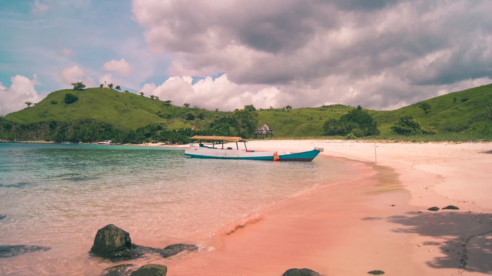 Bateau sur une plage au sable rosé bordée de collines vertes