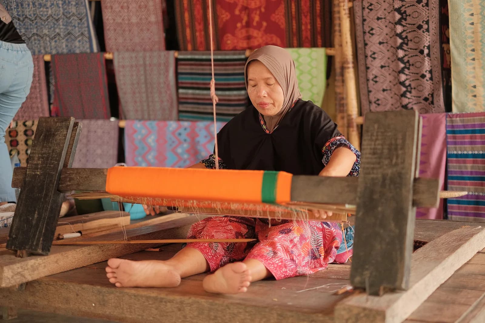 Tisseuse de songket devant son métier à tisser, textiles sasak en fond, Lombok
