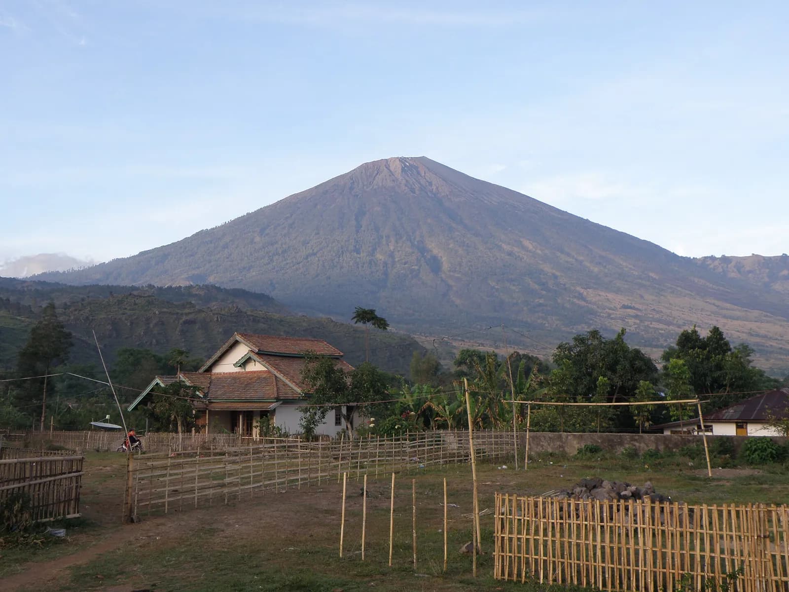 Le cône du mont Rinjani dominant une maison et des clôtures de bambou, à Lombok
