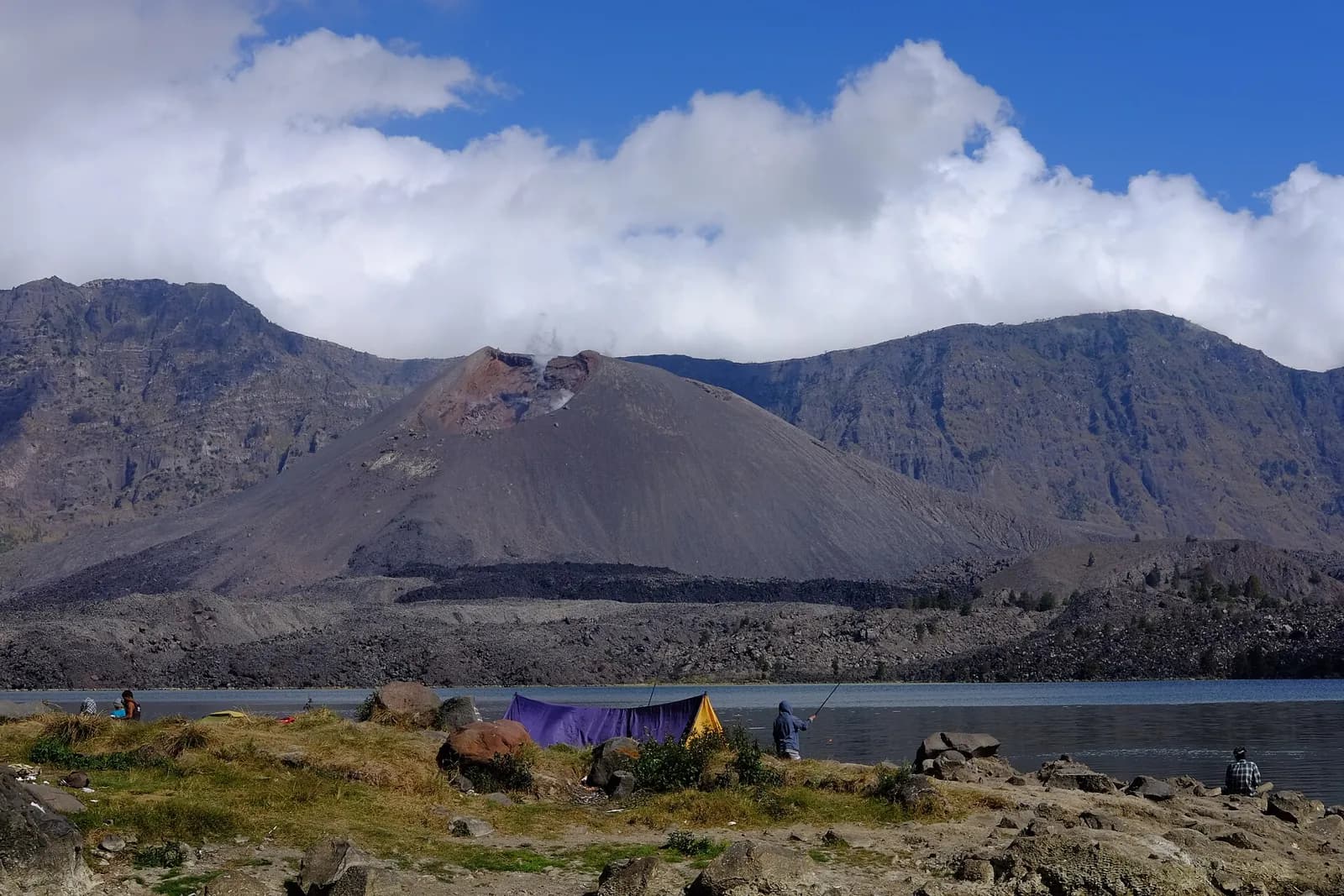 Le cône du Gunung Baru Jari au bord du lac Segara Anak, dans la caldeira du Rinjani, avec une tente et des pêcheurs sur la rive