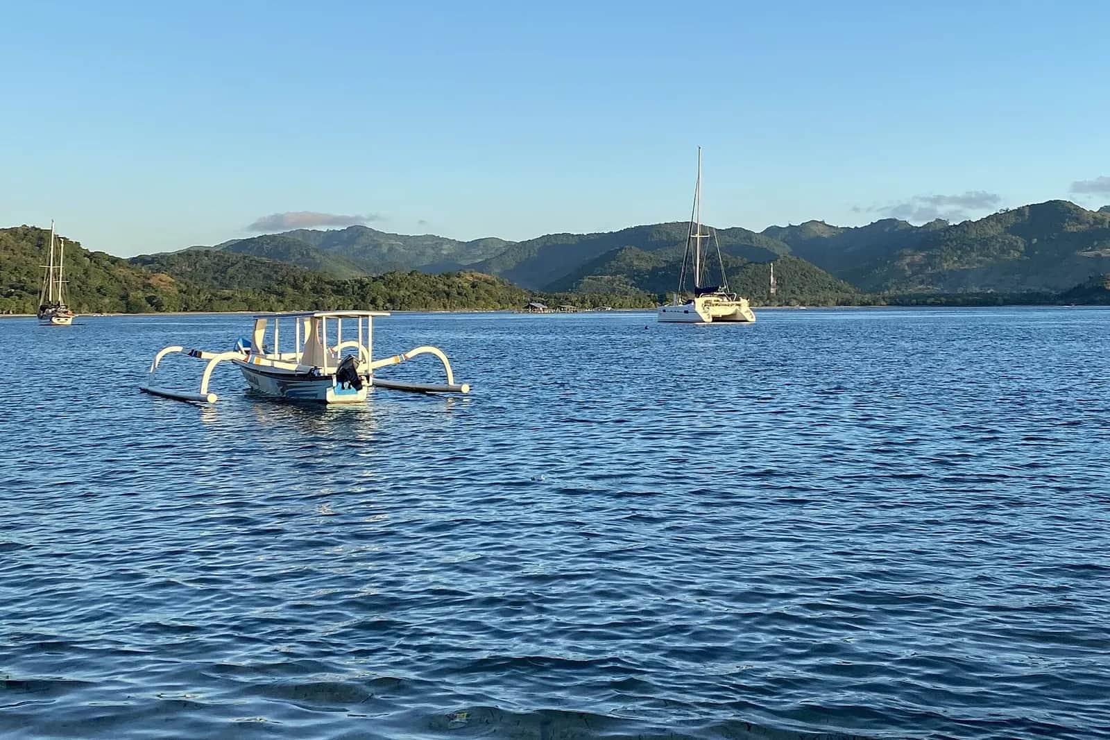 Eau calme, pirogue à balancier et collines de Lombok vues depuis la côte de Gili Asahan