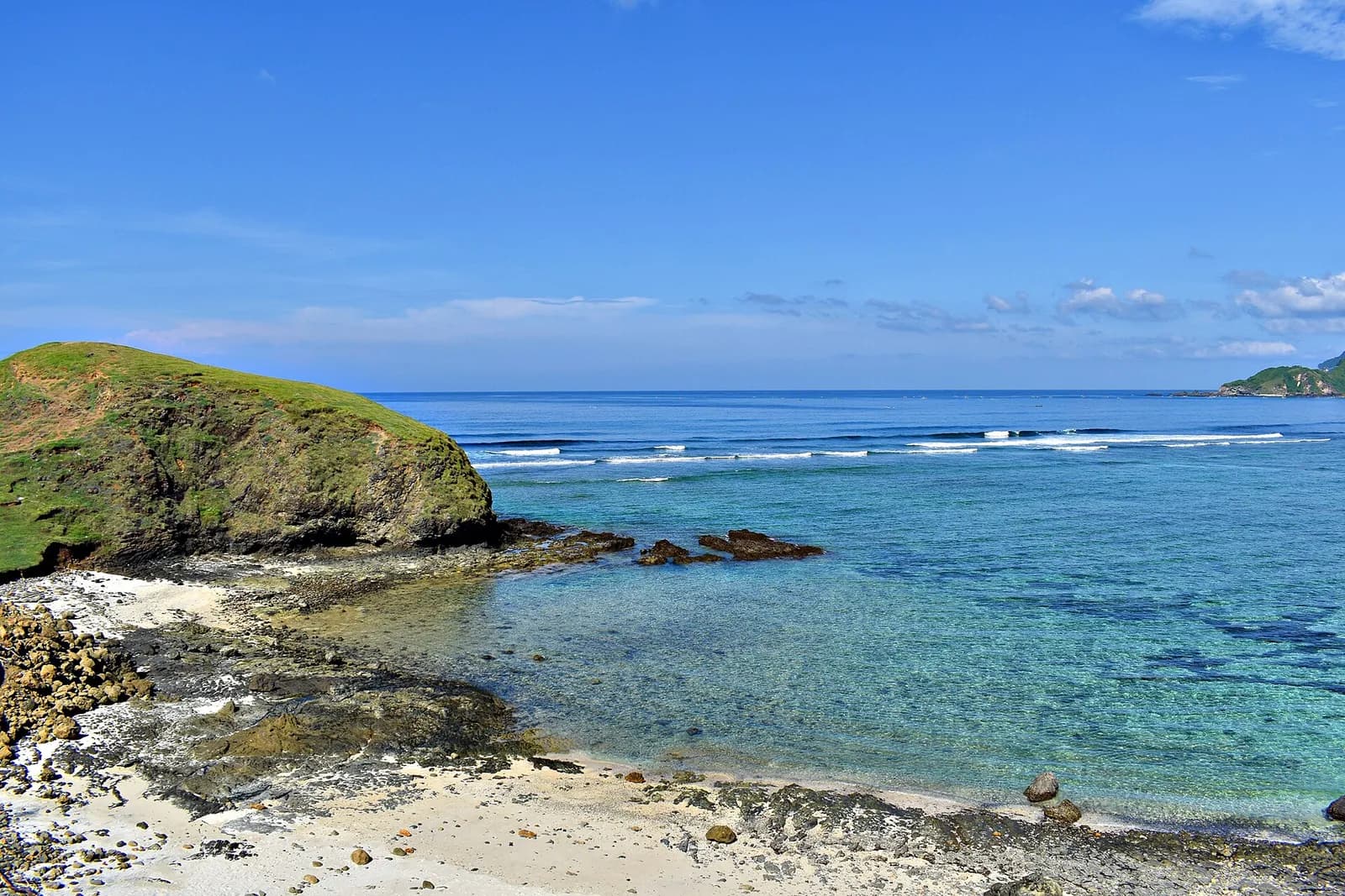 Récif et vagues turquoise au pied d'une colline herbeuse sur la plage de Seger, au sud de Lombok