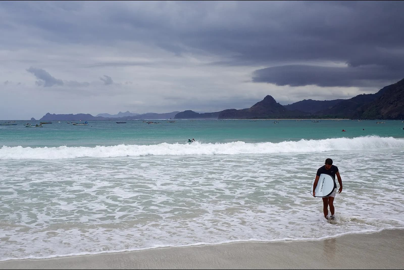 Surfeur sortant de l'eau avec sa planche sur une plage de sable du sud de Lombok