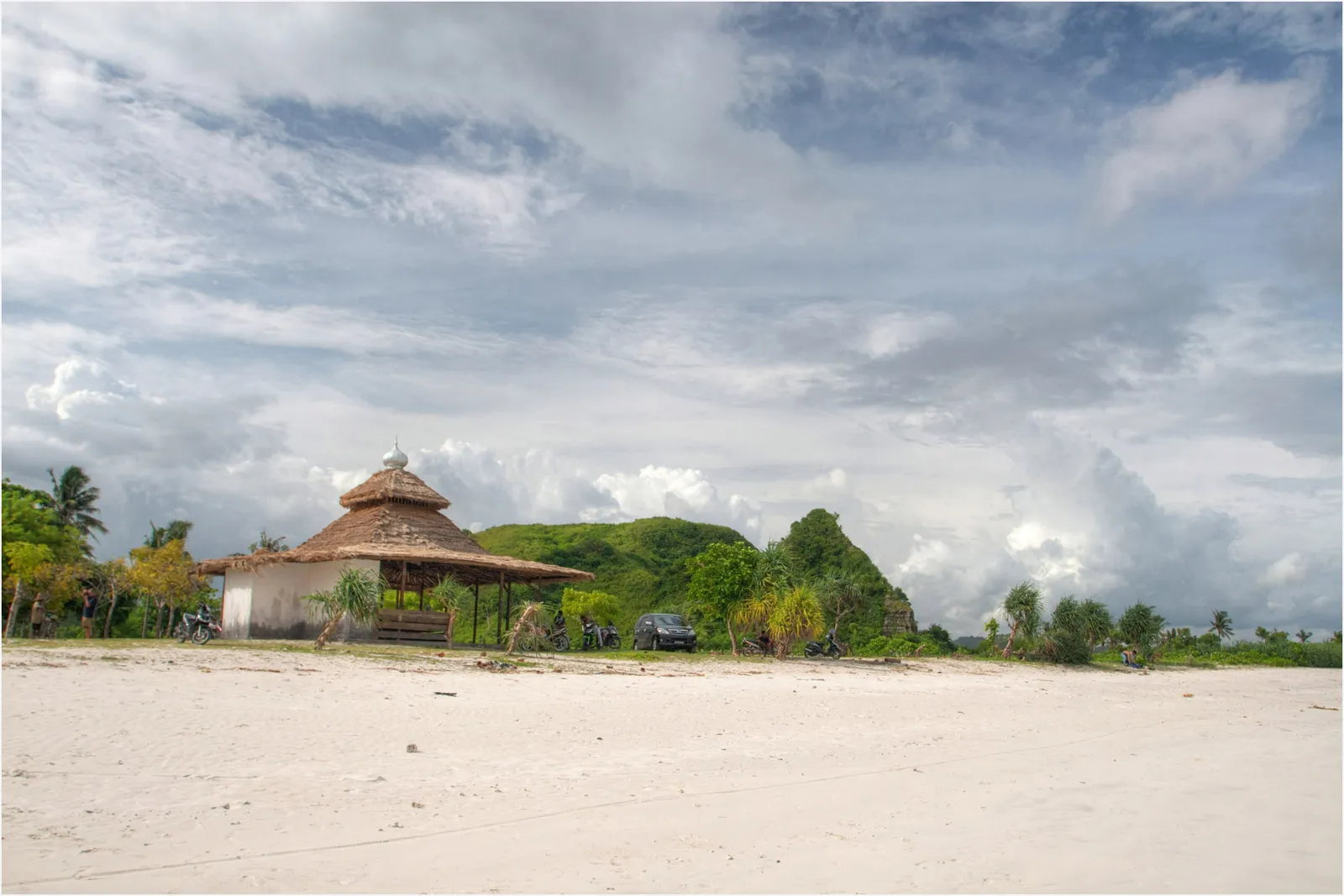 Abri au toit de chaume en haut du sable blanc de la plage de Tanjung Aan, au pied d'une colline verte