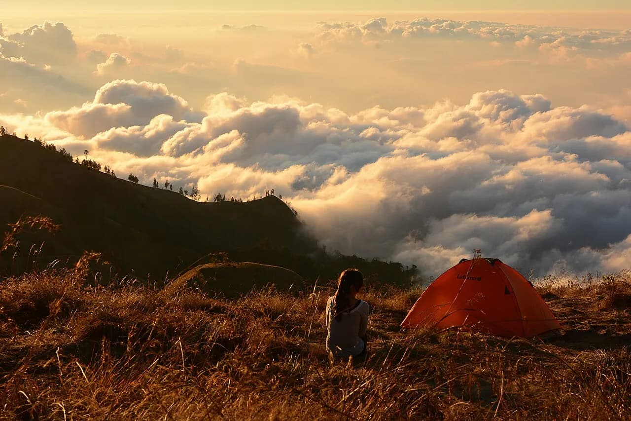 Une tente orange et une randonneuse au-dessus de la mer de nuages, sur les pentes du Rinjani